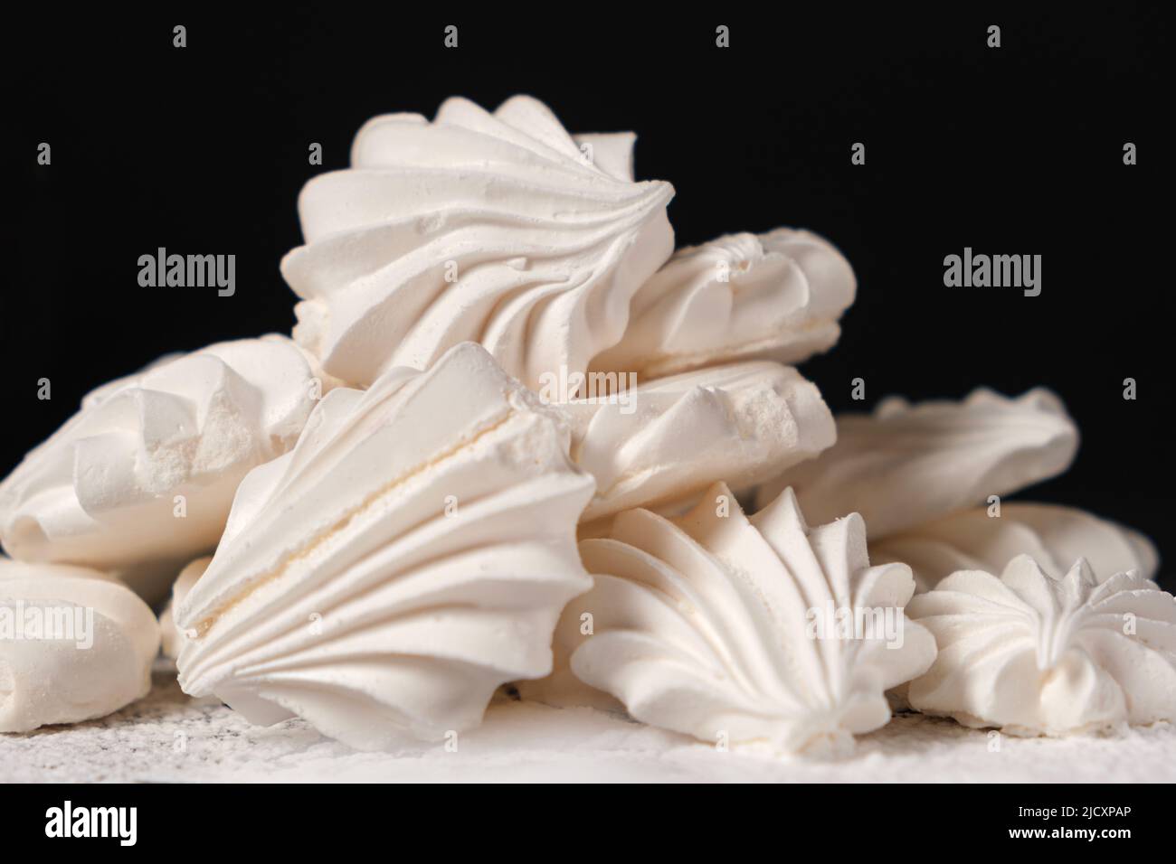 Airy sweet meringue on powdered sugar on a black background closeup
