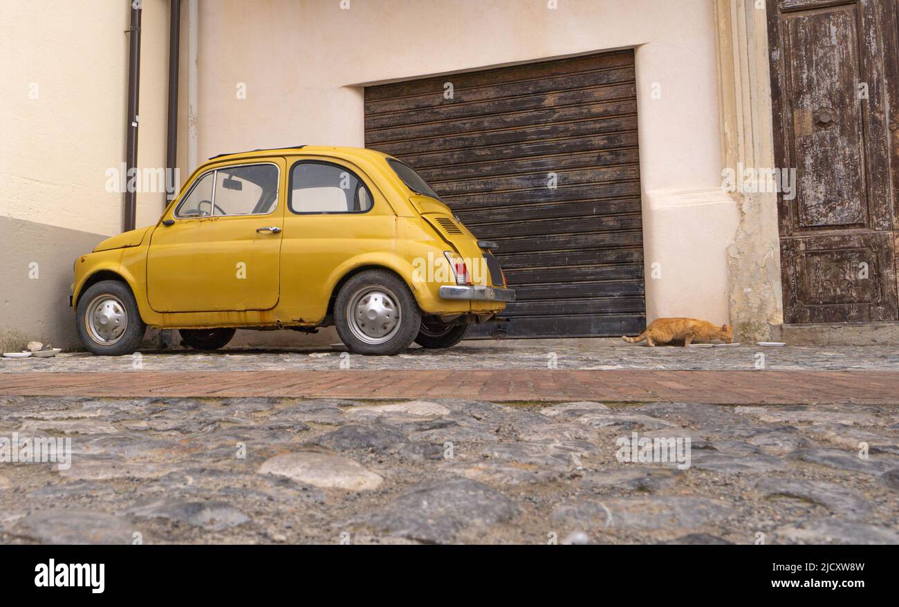 A small yellow vintage car and a cat in front of a house in Italy Stock Photo