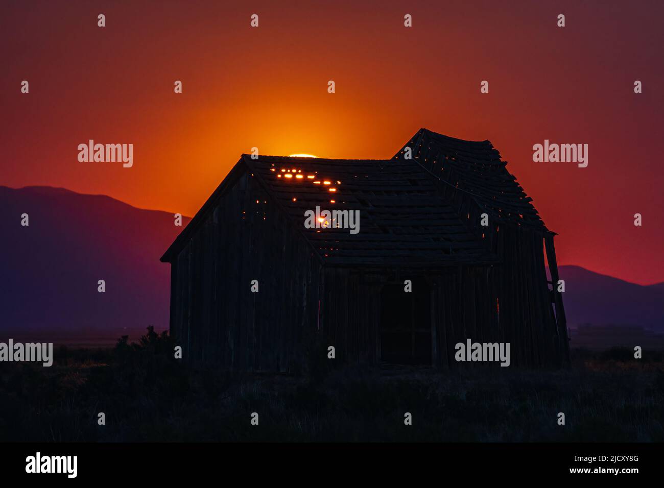 Old barn backlit by a rising full moon casting an eerie orange glow through the slats and silhouetting the building. Stock Photo