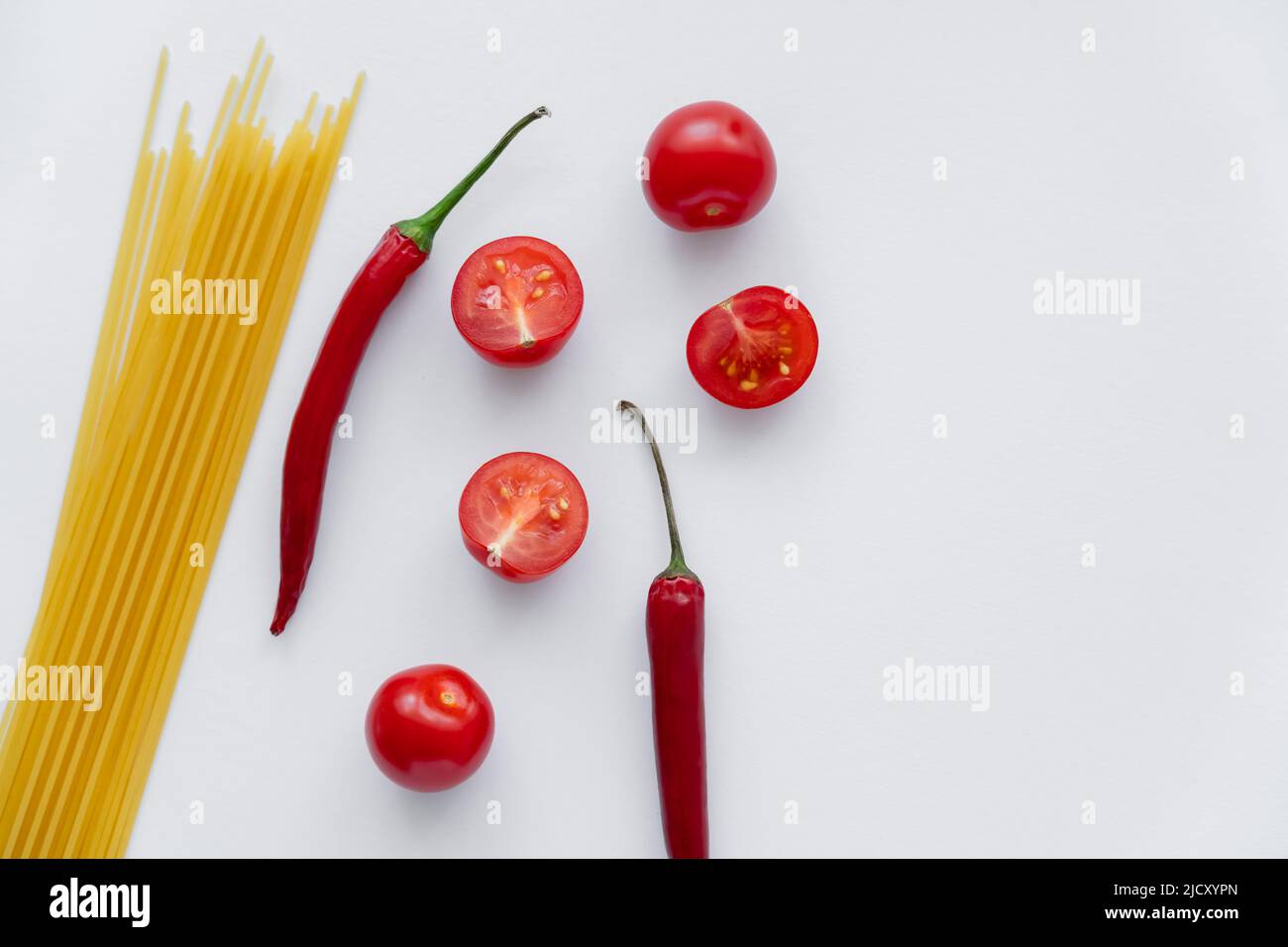 Top view of chili peppers and cherry tomatoes near raw macaroni on