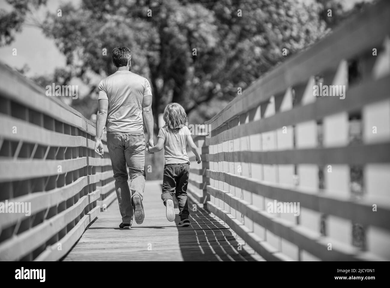 happy father leads with his kid walking outdoor, back view, parenting
