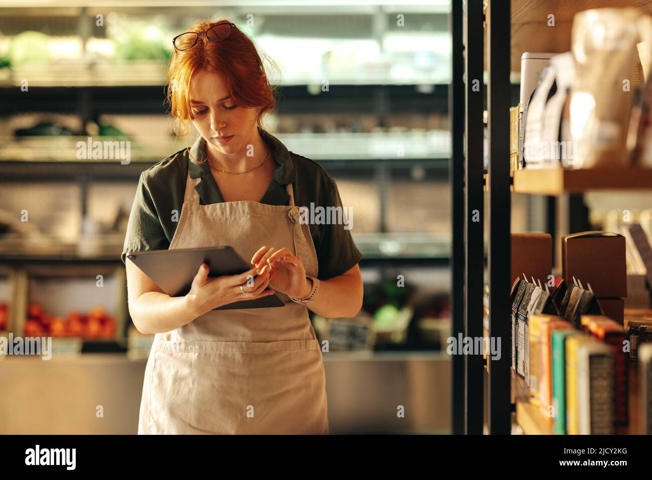 Young shop owner using a digital tablet while standing in her grocery store. Young female entrepreneur running her small business using wireless techn Stock Photo