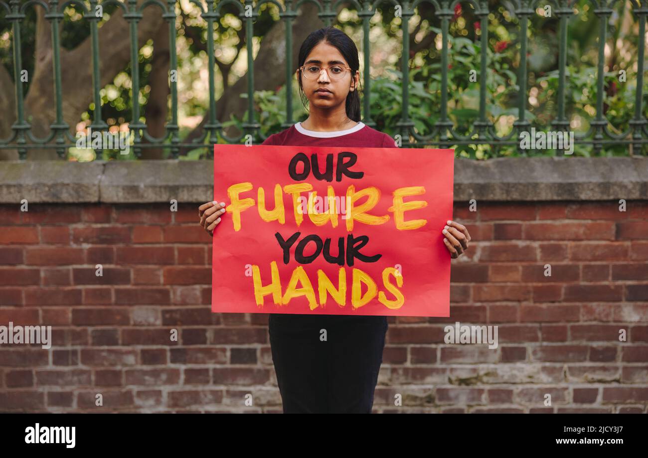 Young teenage girl looking at the camera while holding a climate change poster. Young environmental activist protesting against global warming and cli Stock Photo