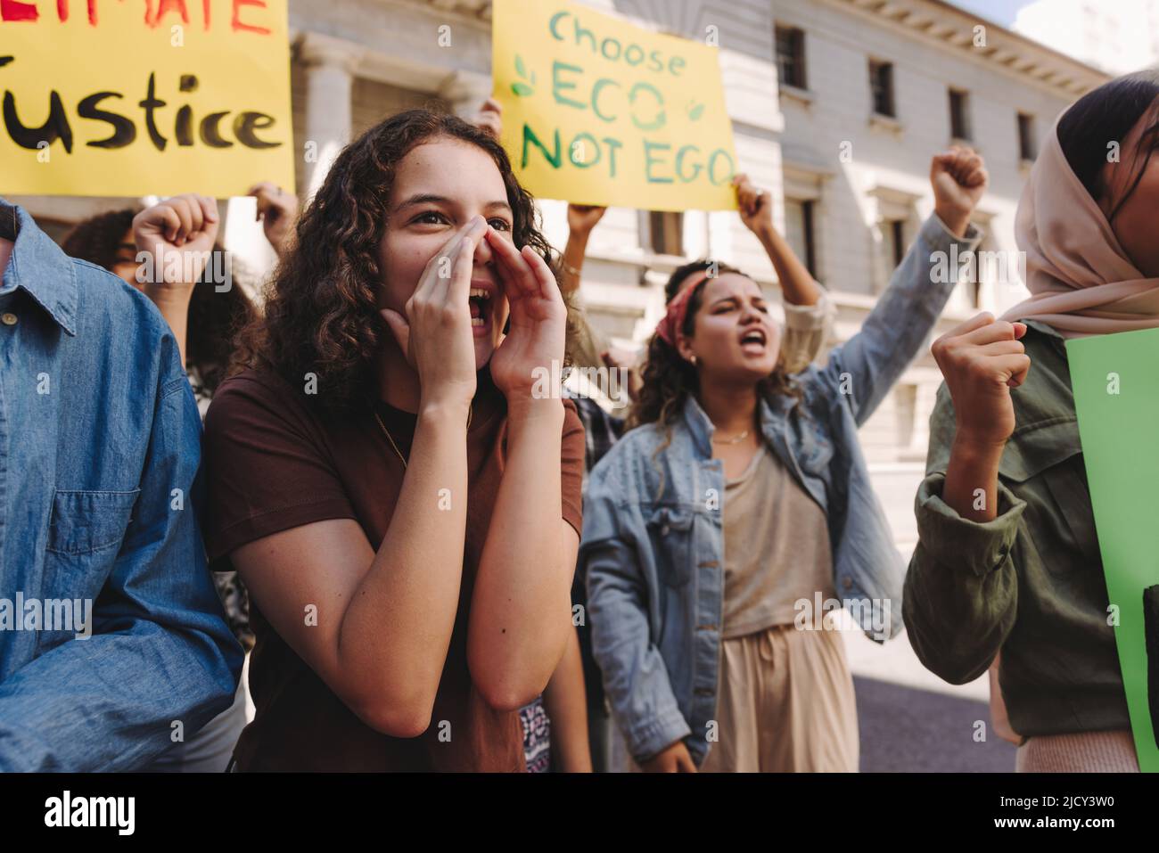 Vibrant climate change activists raising banners and shouting slogans while protesting in the city. Group of multicultural young people marching for c Stock Photo