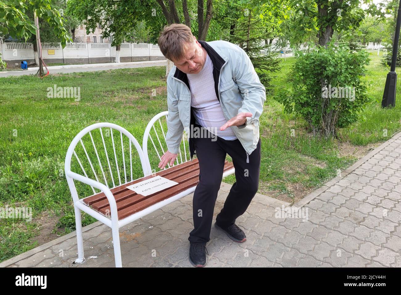An adult man soiled his clothes and hands painted bench in the park, The inscription on the paper is carefully colored. Stock Photo