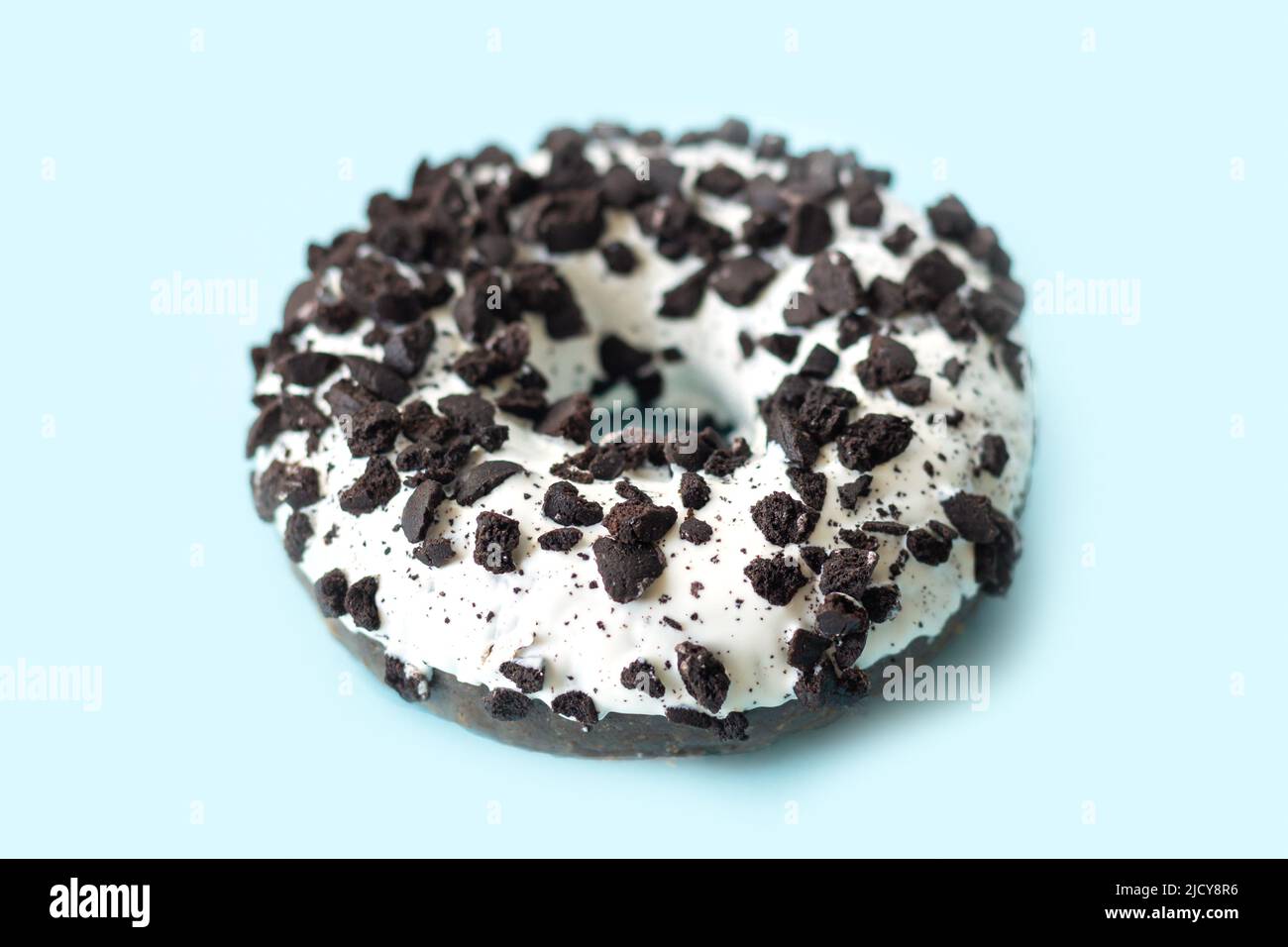 Tasty white chocolate glazed donut with dark cookies crumbs on light blue background Stock Photo