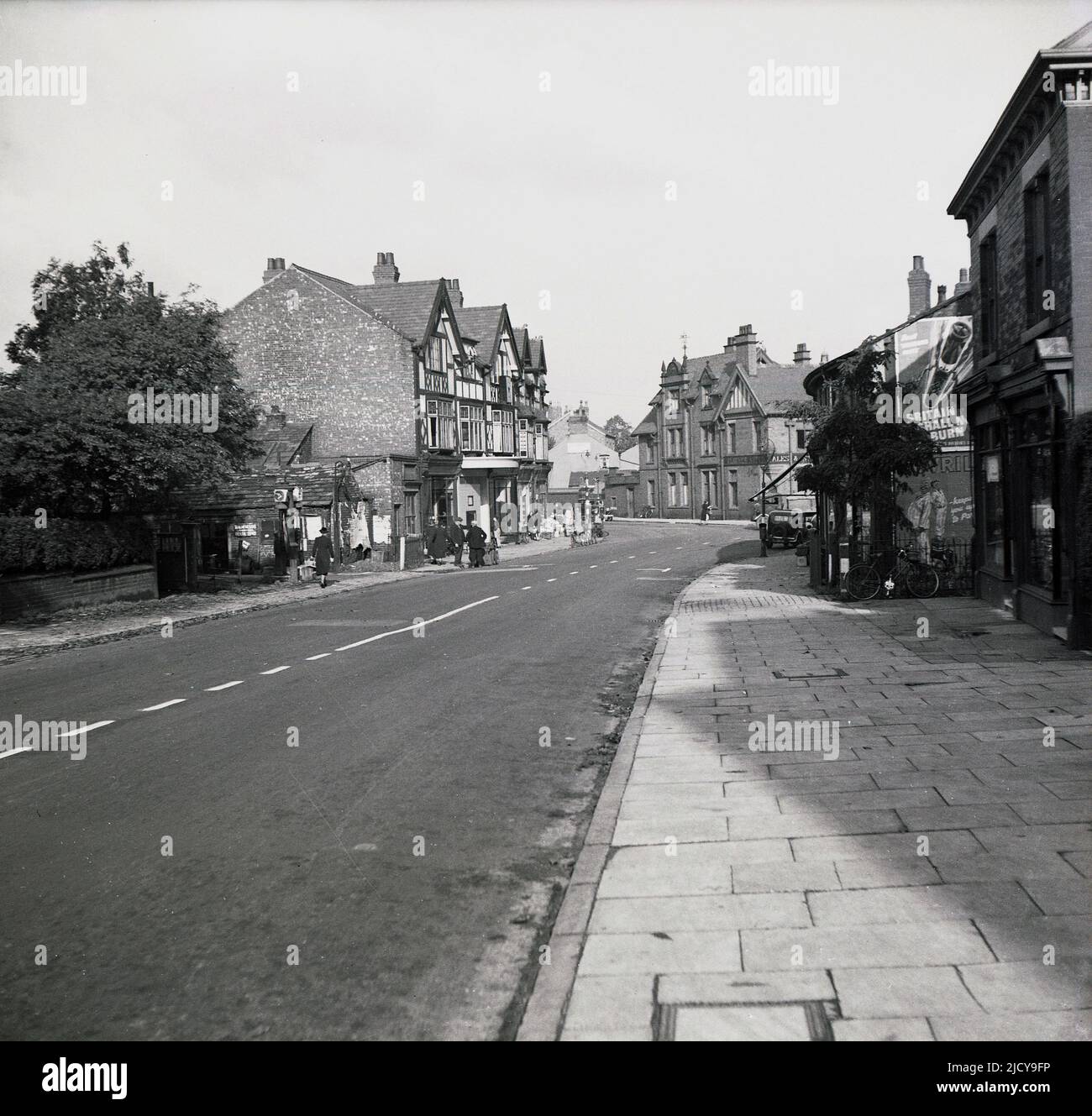 1940, historical, view from the south of the village of Bramhall, a suburb of Stockport, Greater Manchester, England, UK. On the right, a building with a poster, 'Beat Firebomb Fritz' - 'Britain Shall Not Burn' with a picture of a Nazi rocket. During WW2 the Ministry of Home Security commissioned artist Fritz Rosen to produce posters which reassured the public about the Blitz, the Nazi bomb campaign of 1940-1941. Rosen created a cartoon character known as ‘Firebomb Fritz’ that was shaped like a German incendiary bomb with an angry looking face. Stock Photo