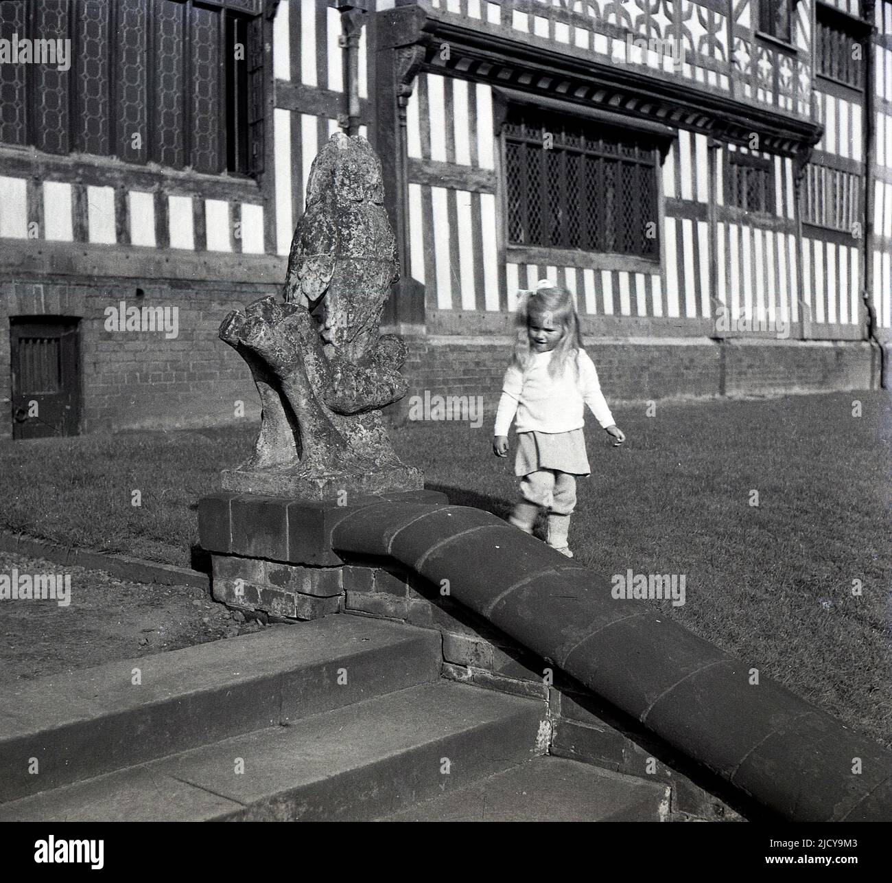 1940s, historical, a little girl by the steps outside the front of Bramall Hall, Bramhall, Stockport, England, UK. A timber-framed Tudor manor house that dates back to the 14th century, with later additions, the house and surrounding parkland was acquired by the local authority in 1935 and became a museum. The Davenport family, which it is believed built the house, held the manor for over 500 years. Stock Photo