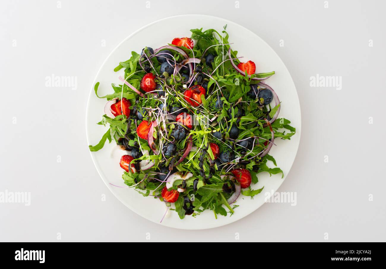 Light salad with arugula and berries, strawberries and blueberries, delicious healthy summer salad on a white background Stock Photo