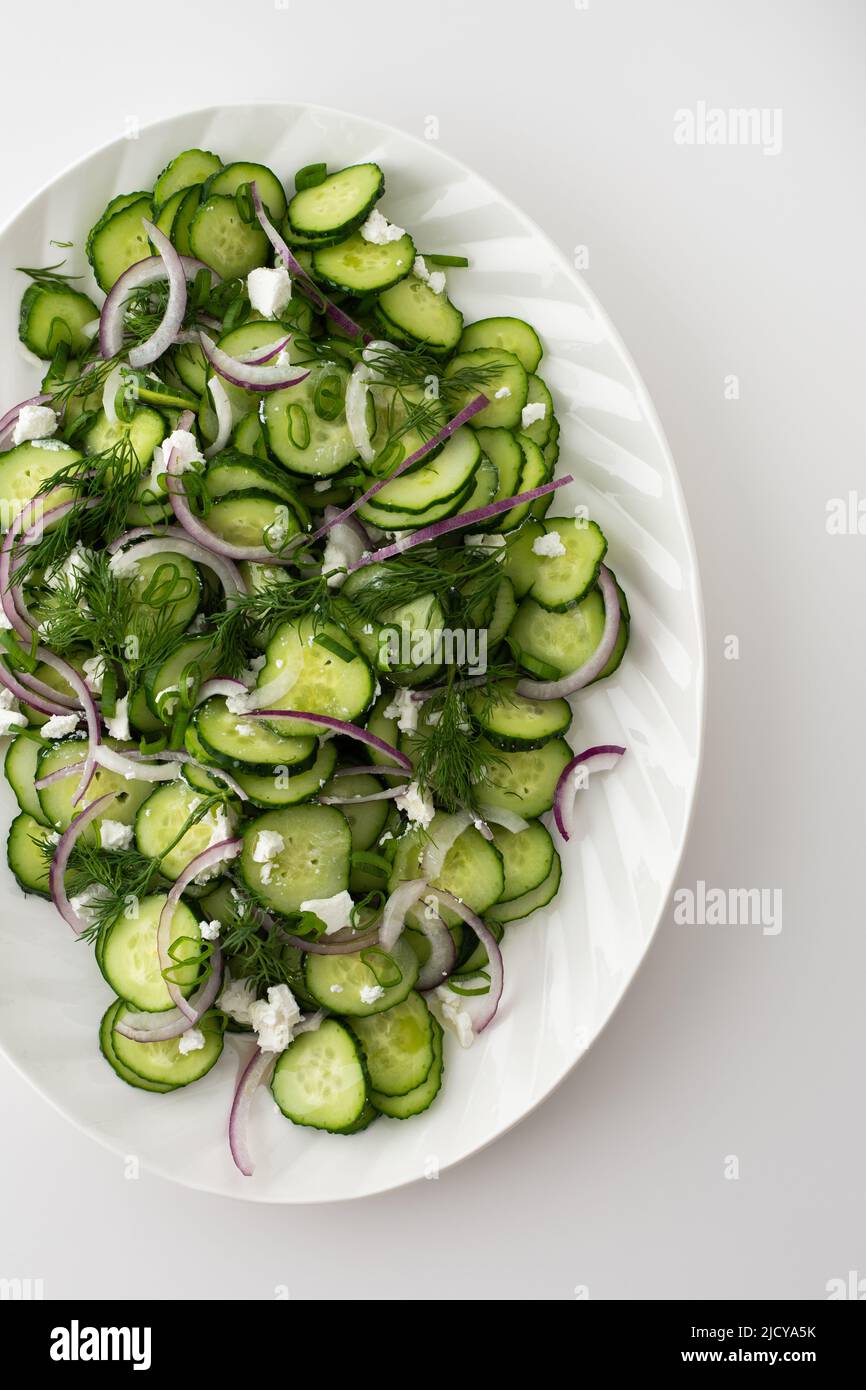 Light summer salad of cucumbers, onions and feta cheese in an oval white dish, top view Stock Photo