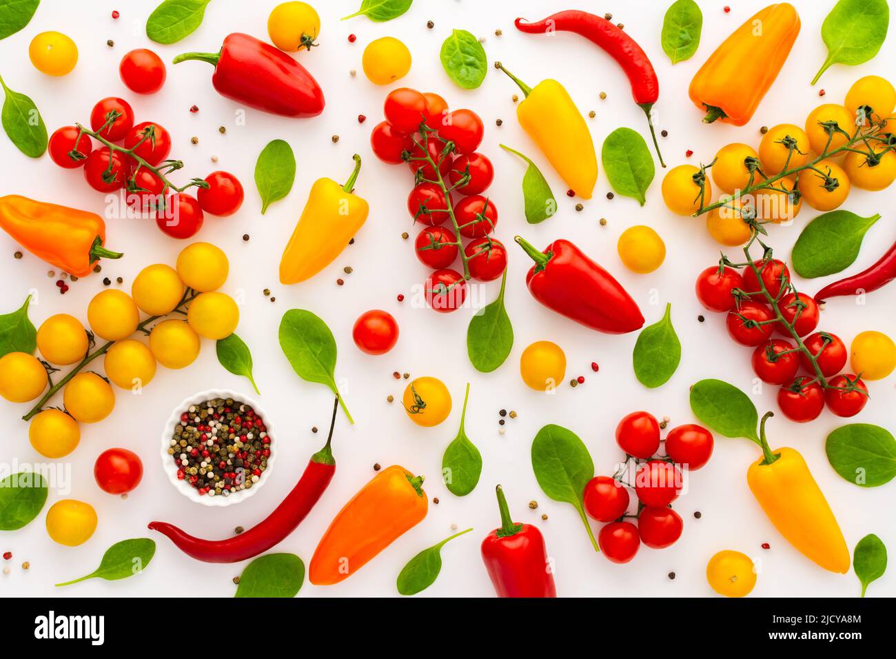 Yellow and red tomatoes, hot peppers, spinach and spices on a white background, food background, top view Stock Photo