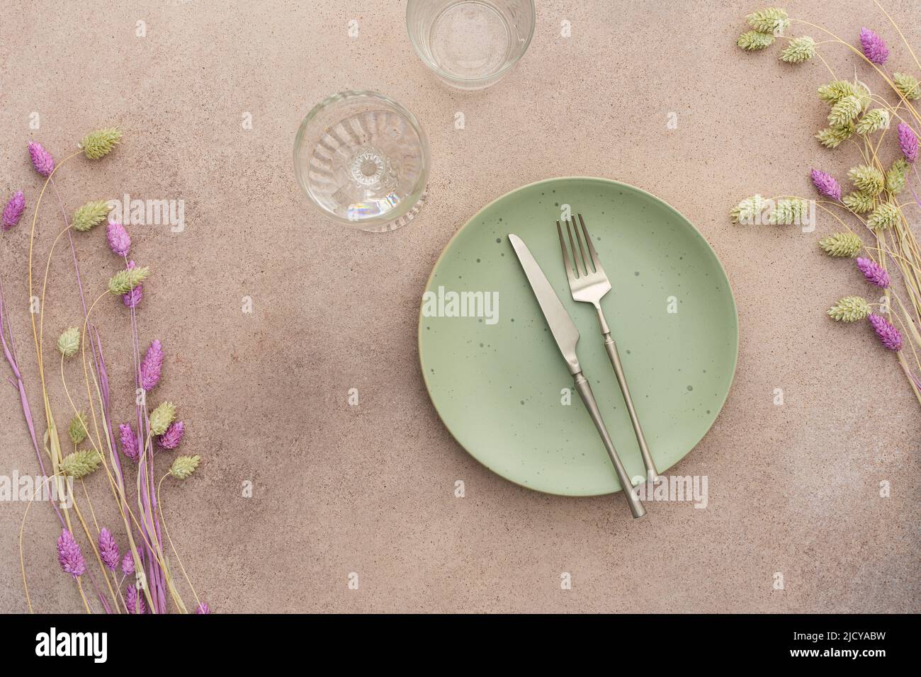 Table setting, empty green plate and cutlery on a concrete background, top view of the served table decorated with dry flowers Stock Photo