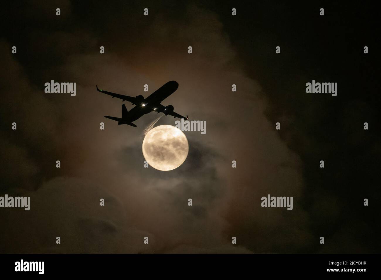 Aircraft flying in path of full moon at night Stock Photo