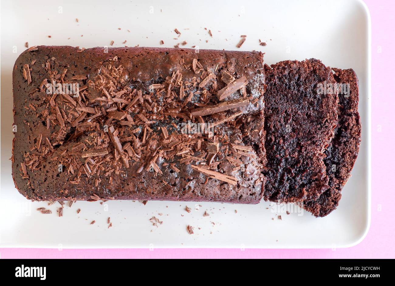 A rich delicious quadruple chocolate loaf cake freshly home baked and sat  on a plate. Two slices have but cut showing the moist chocolate centre Stock Photo