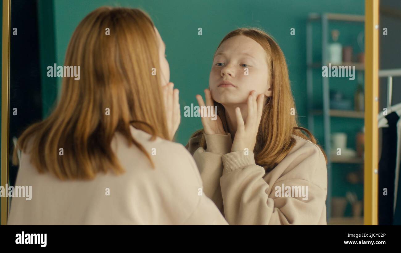 Depressed Red haired Teenage Girl Looking at Her Reflection in the Mirror. Stock Photo