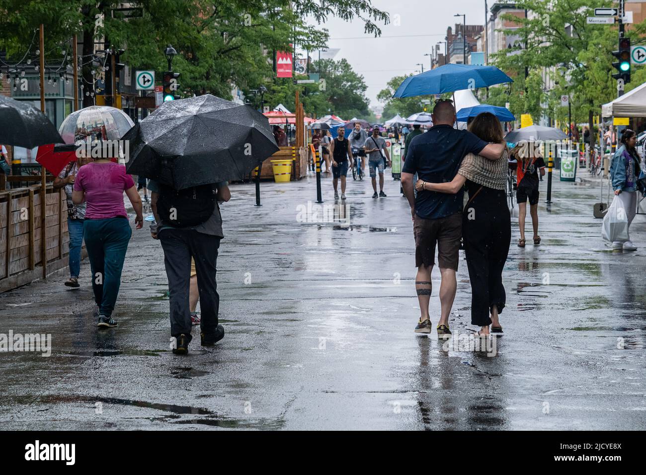 Montreal, CA - 12 June 2022: People on Mont-Royal Avenue holding umbrella during rain & storm Stock Photo