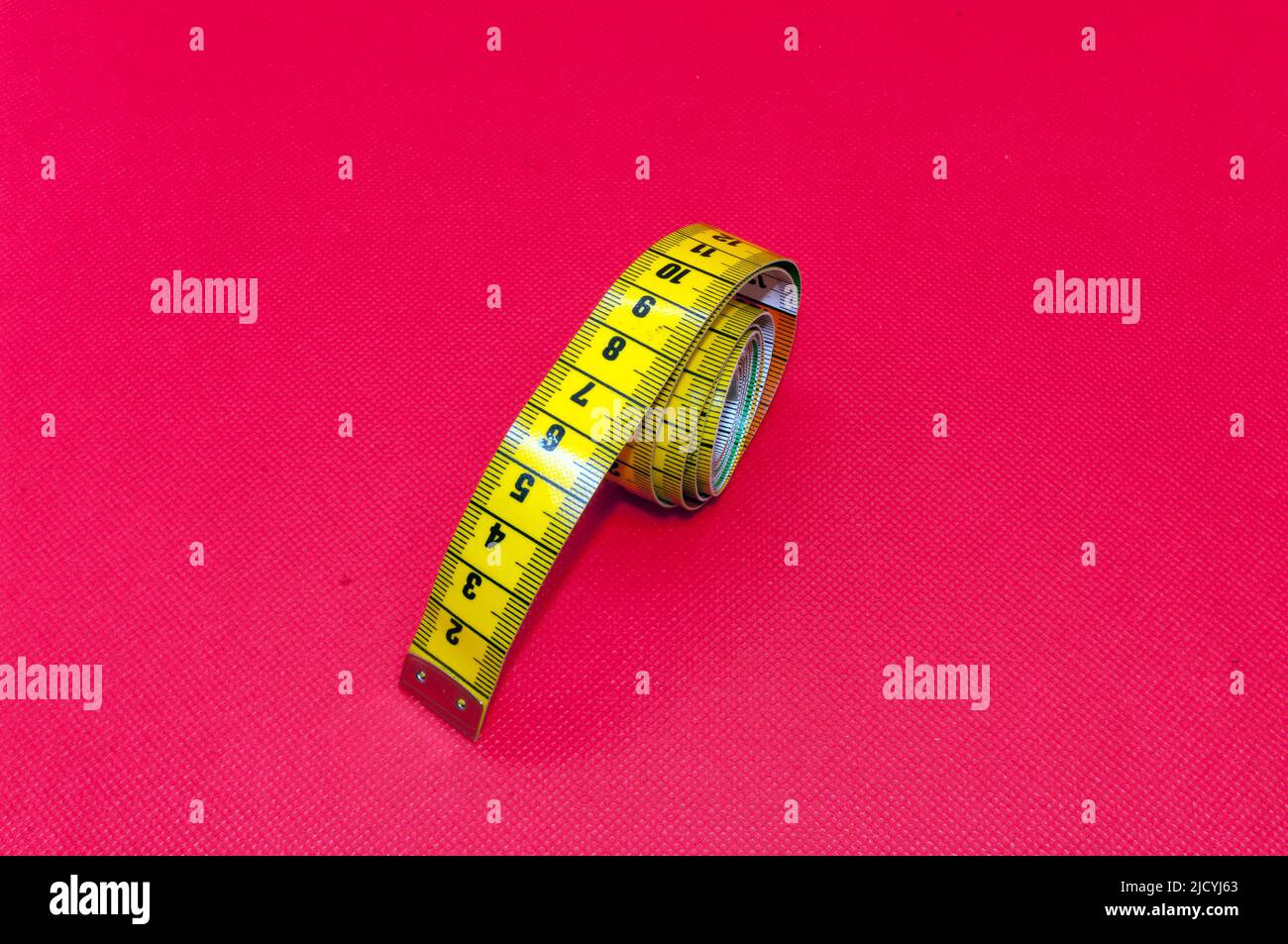 Iconic picture measure: flexible tailor's tape measure, isolated against red background Stock Photo