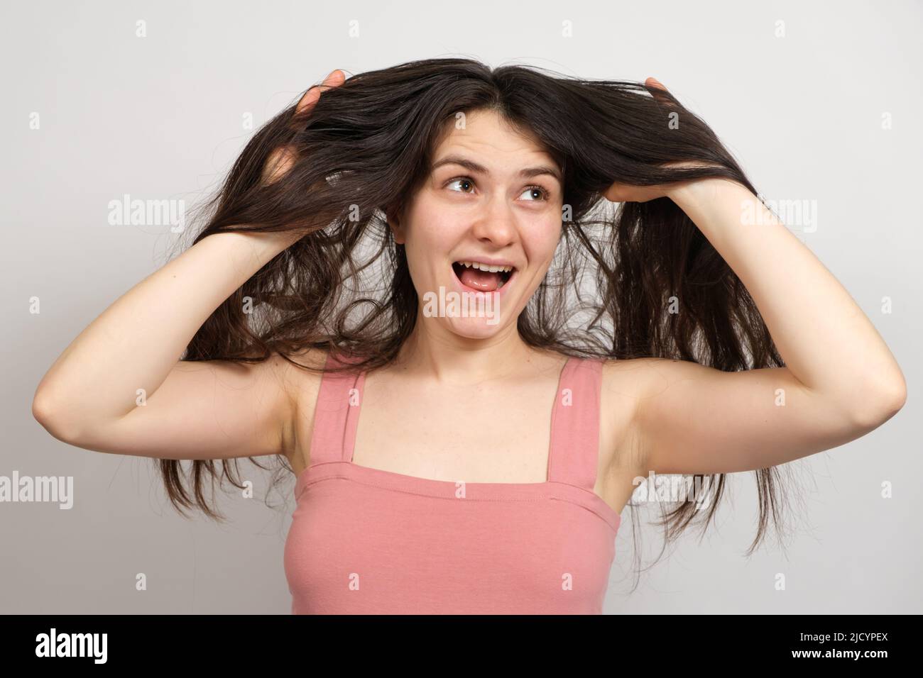 A beautiful brunette woman with long hair on a white background holds her hands on her head and thinks about what hairstyle to do Stock Photo