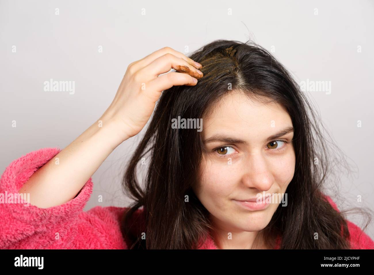 A brunette woman applies a natural Ayurvedic blend of herbs to her hair, scalp mask and scrub, hair care at home. Stock Photo