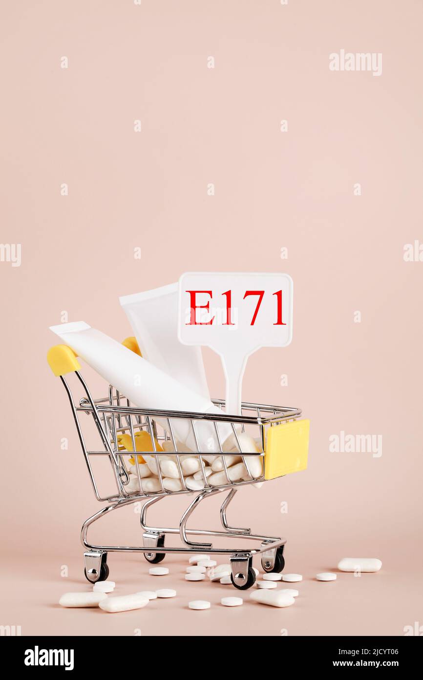 Titanium dioxide, E171, dangerous additive concept. gum, pills, toothpaste, cream in basket and sign with E171 on beige background. copy space Stock Photo