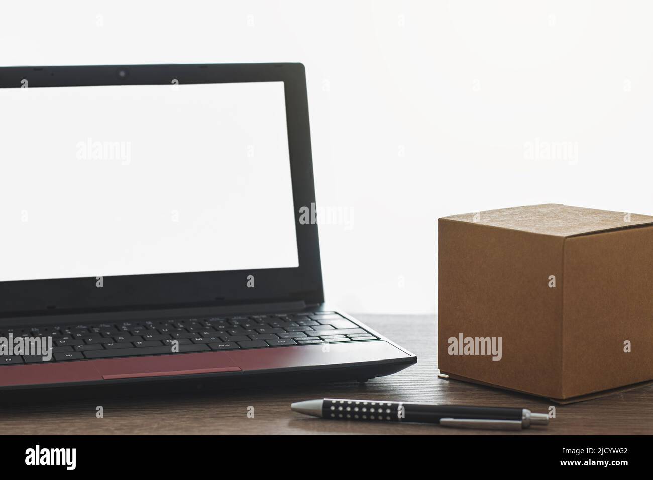 On a wooden table is a small cardboard box and a pen next to a laptop ...