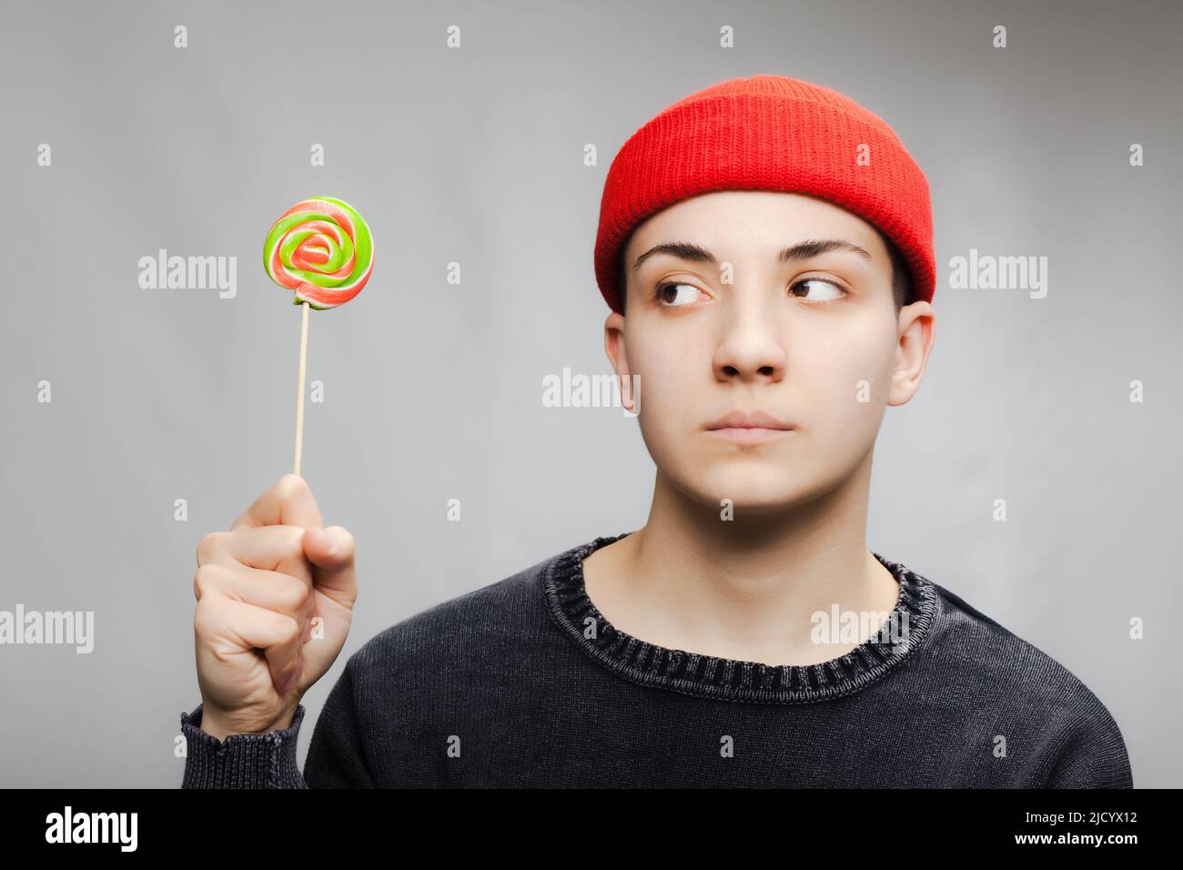 Girl with short hair and a lollipop wearing blouse and red hat against gray background. Stock Photo