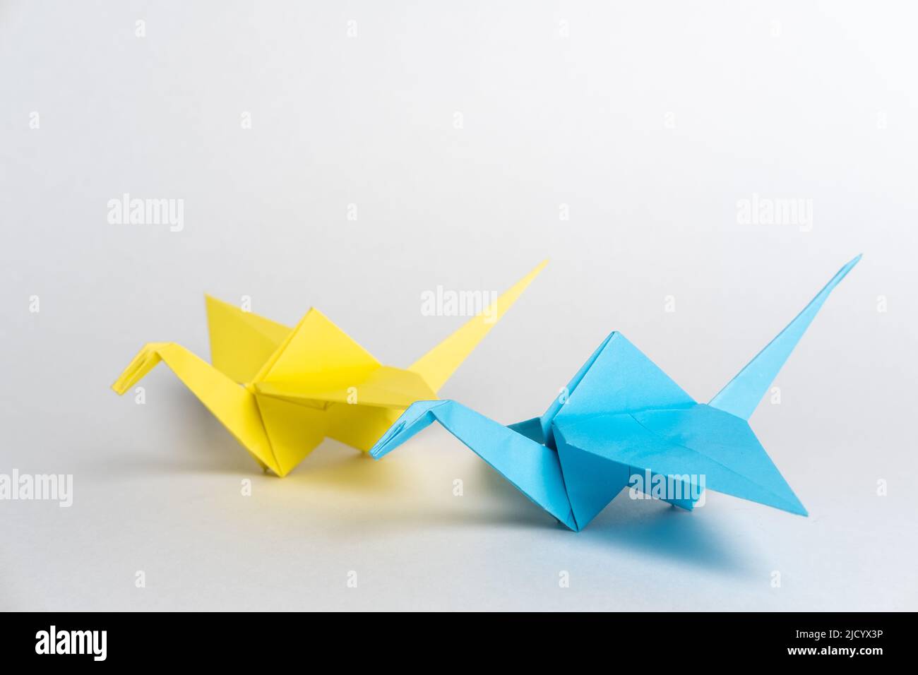 Traditional Japanese origami cranes made of blue and yellow paper on a white background. Pair of