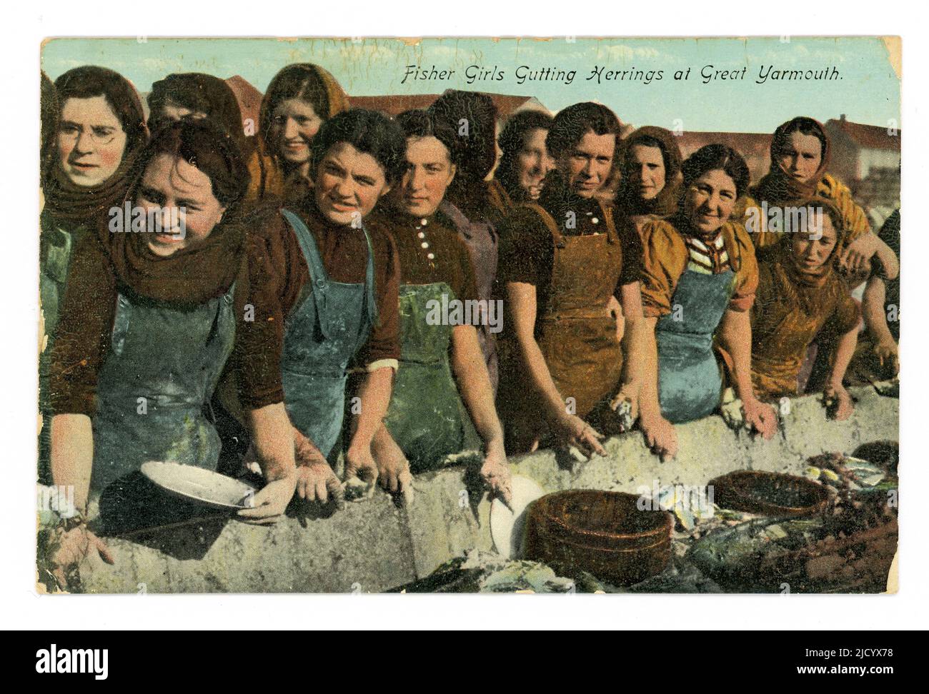 Original early 1900's photograph, circa 1919, tinted/colourised and still being printed in the 1930's - a postcard of cheerful fisher girls gutting herrings at Great Yarmouth, these were probably Scottish seasonal migrant labourers. The gutters worked at long troughs called farlins or farlans and had to sort the herring by size and quality. The postcard was posted in June 1931, Great Yarmouth, Norfolk, England,  U.K. Stock Photo