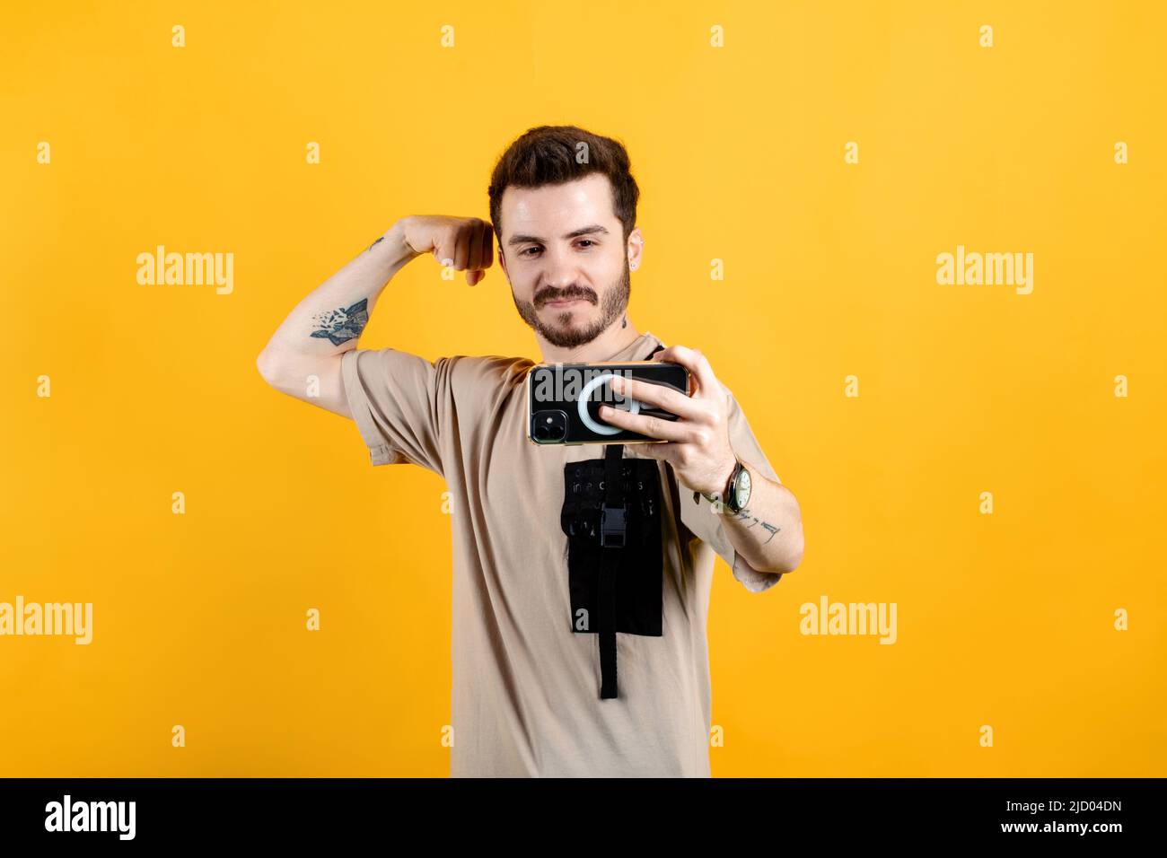 Handsome young man wearing casual clothes posing isolated over yellow background taking selfie, showing strong arm, flexing biceps and posing for phot Stock Photo