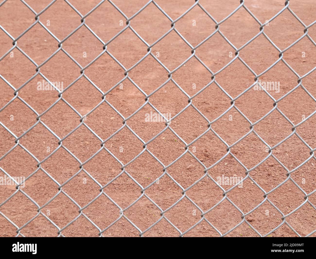 Close up of a chain-link fence with light brown dirt background Stock Photo