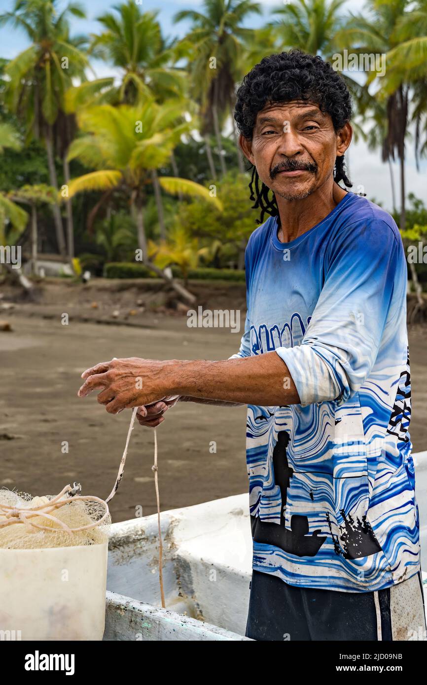 Man looking at the camera preparing his net to fish in his boat with palm trees in the background. Stock Photo