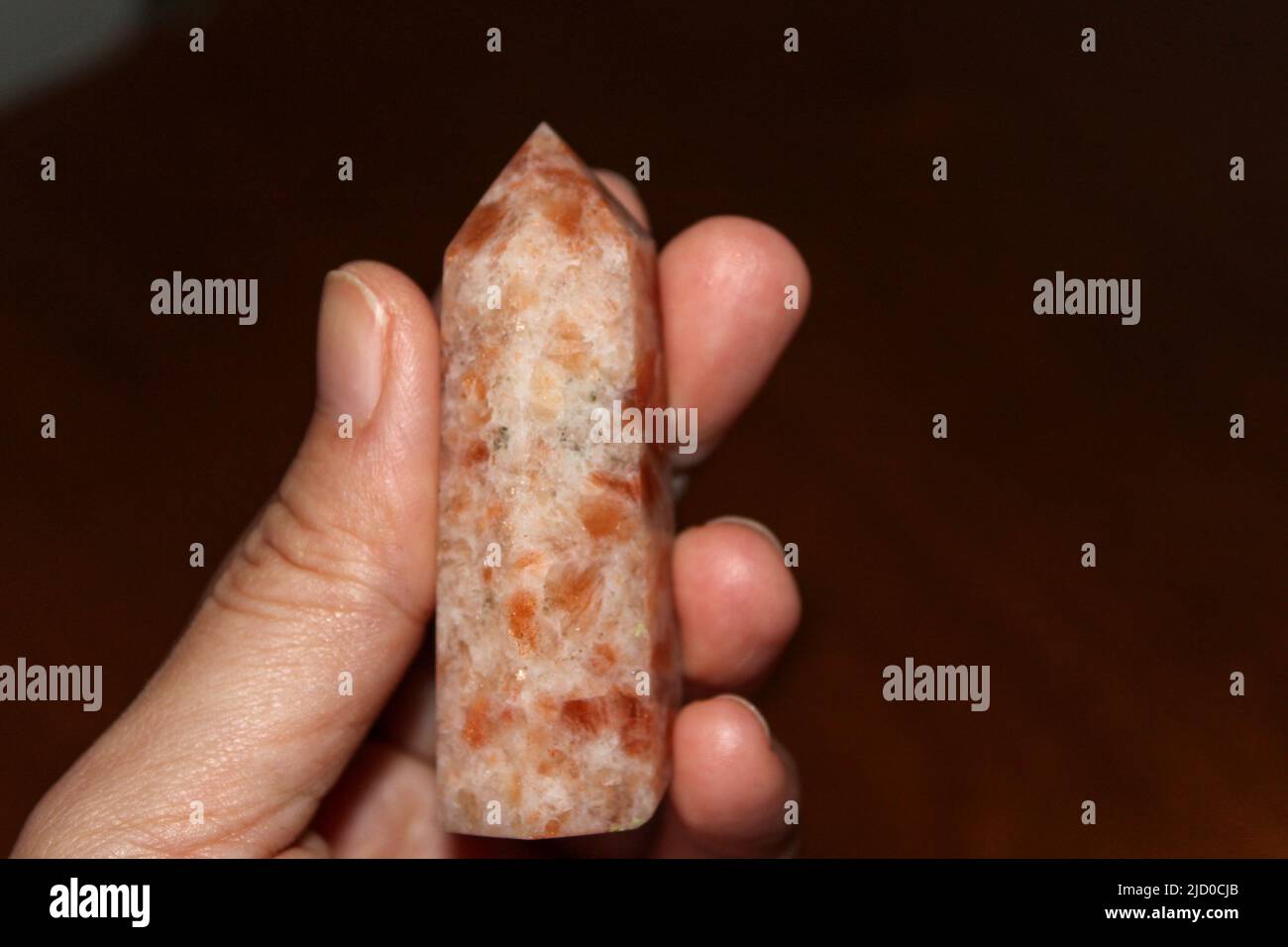 Person holding a polished sunstone point also known as a sunstone tower crystal. Sunstone is a healing stone that works across the physical, spiritual Stock Photo