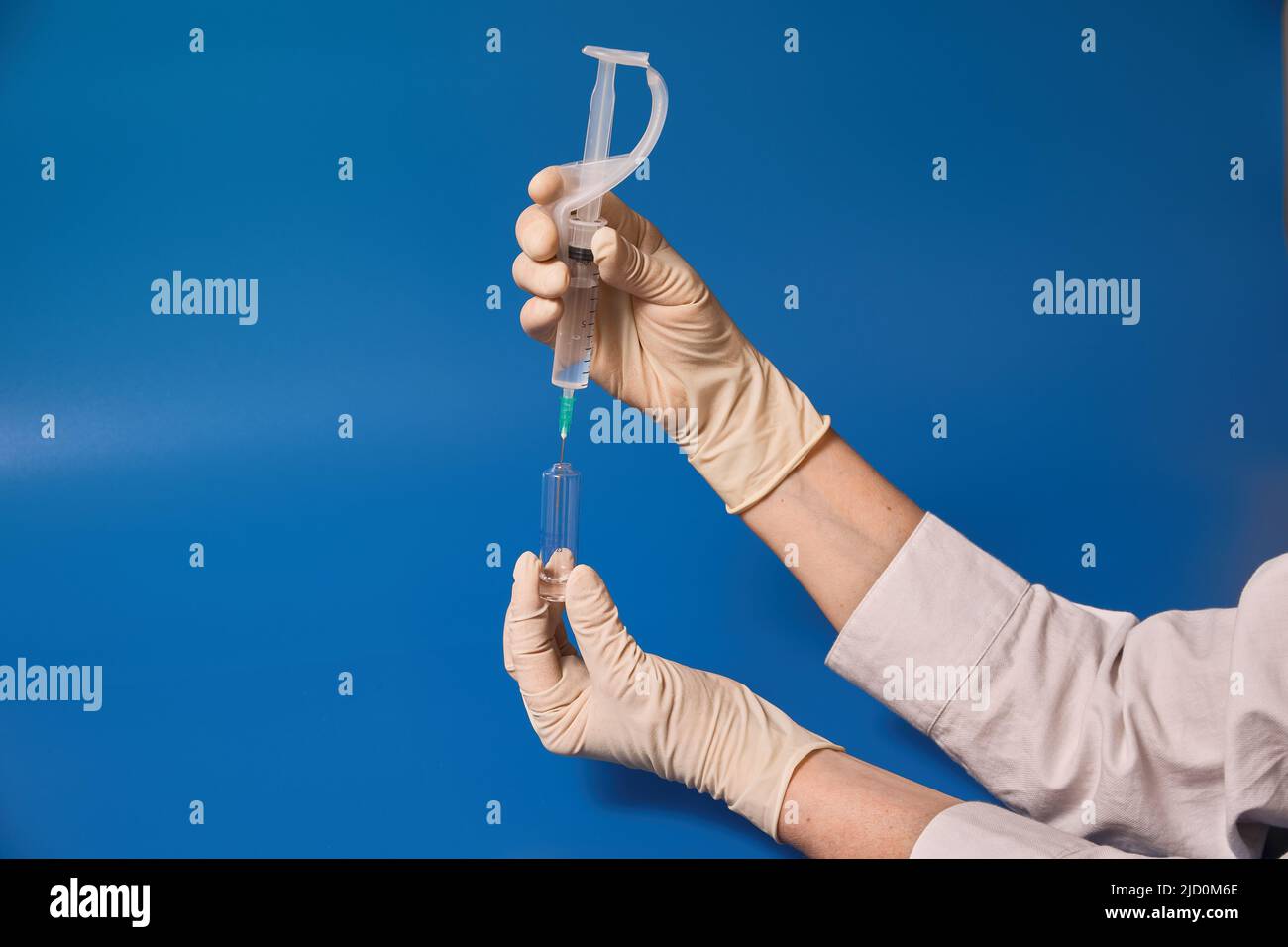 Gloved hand holding syringe on blue background  Stock Photo