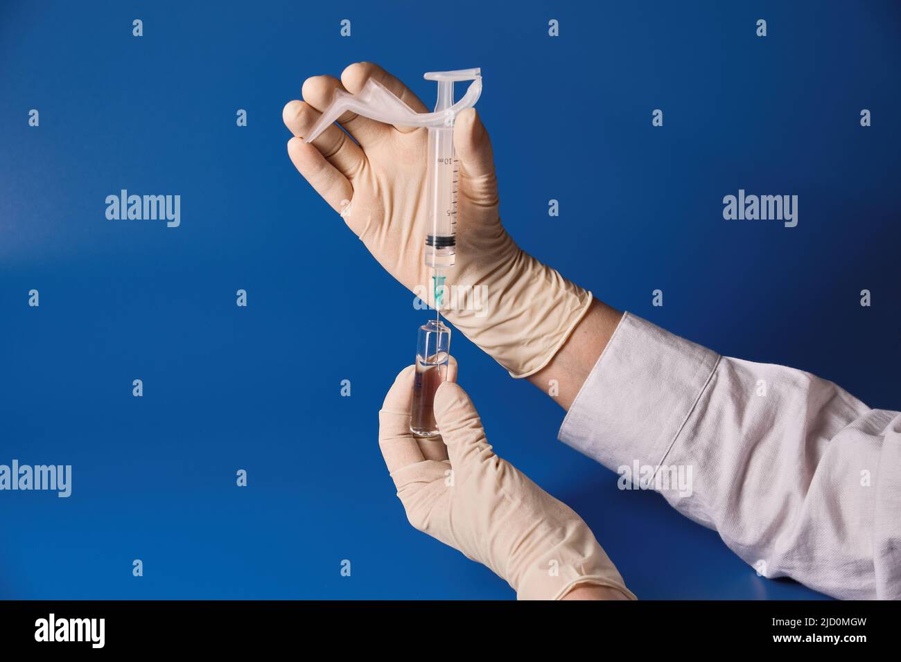 Gloved hand holding syringe on blue background  Stock Photo