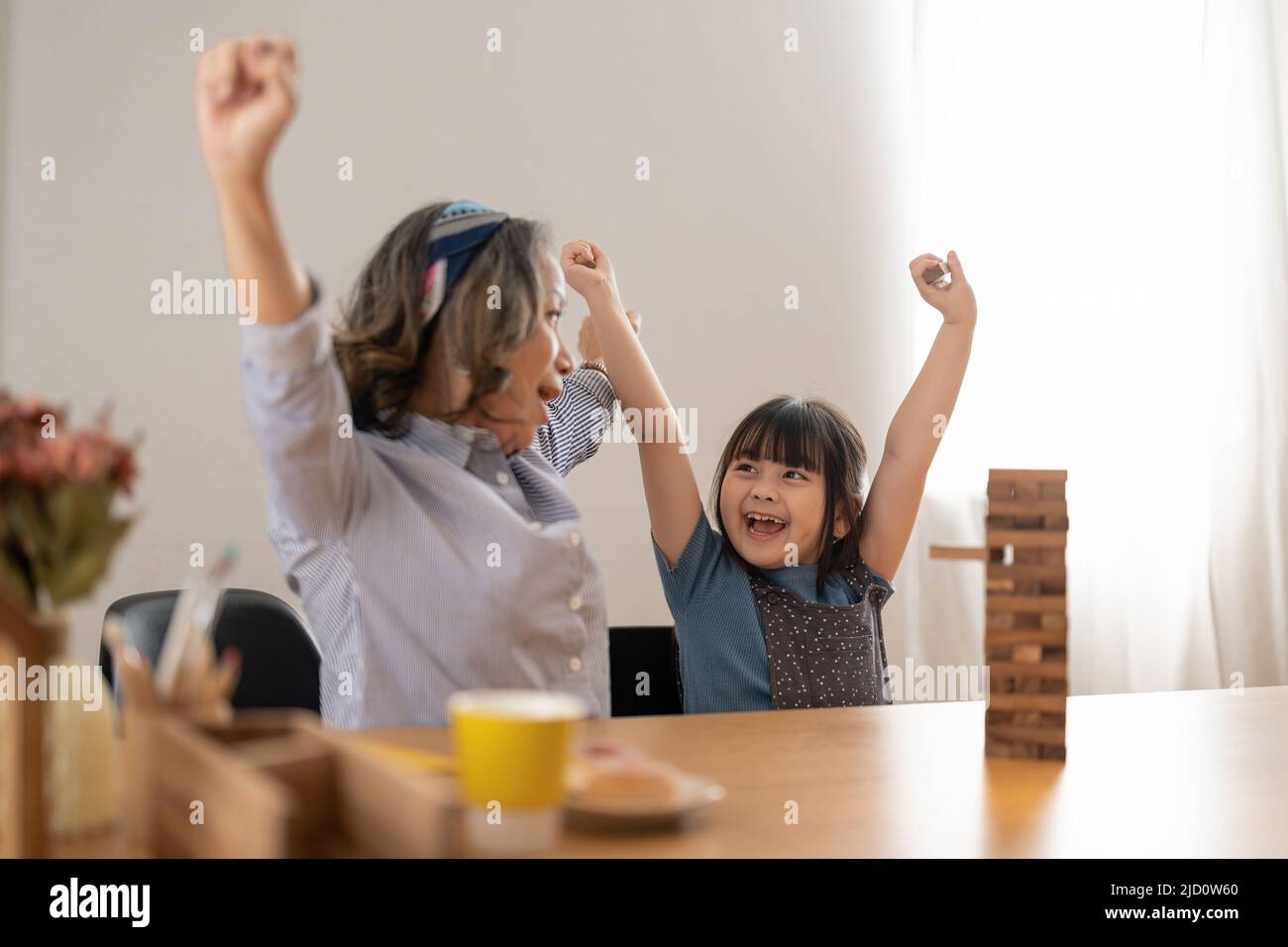 Happy moments of Asian grandmother with her granddaughter playing jenga constructor. Leisure activities for children at home. Stock Photo