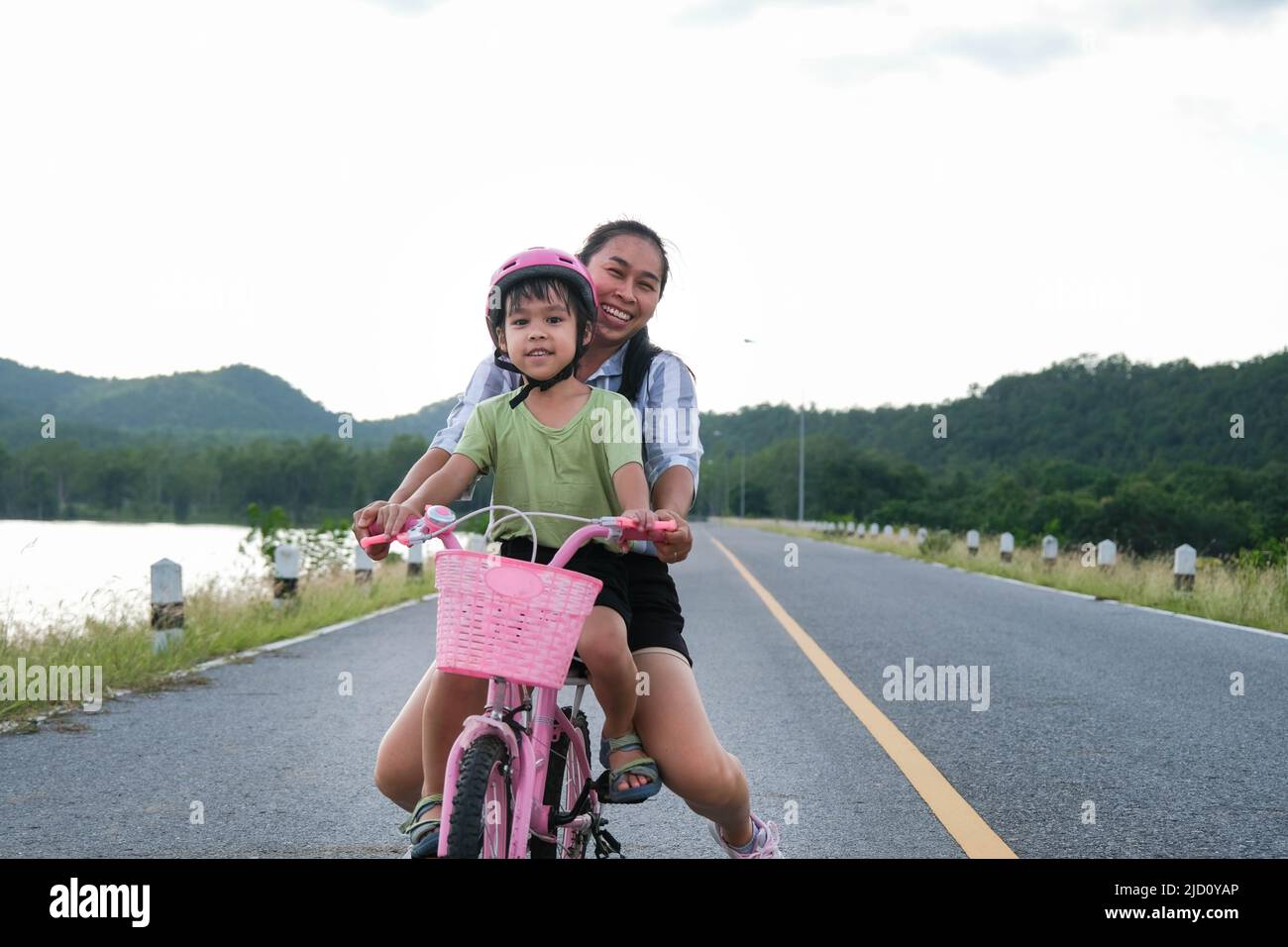 Cute little girl riding a bicycle with her mother on a lake road at