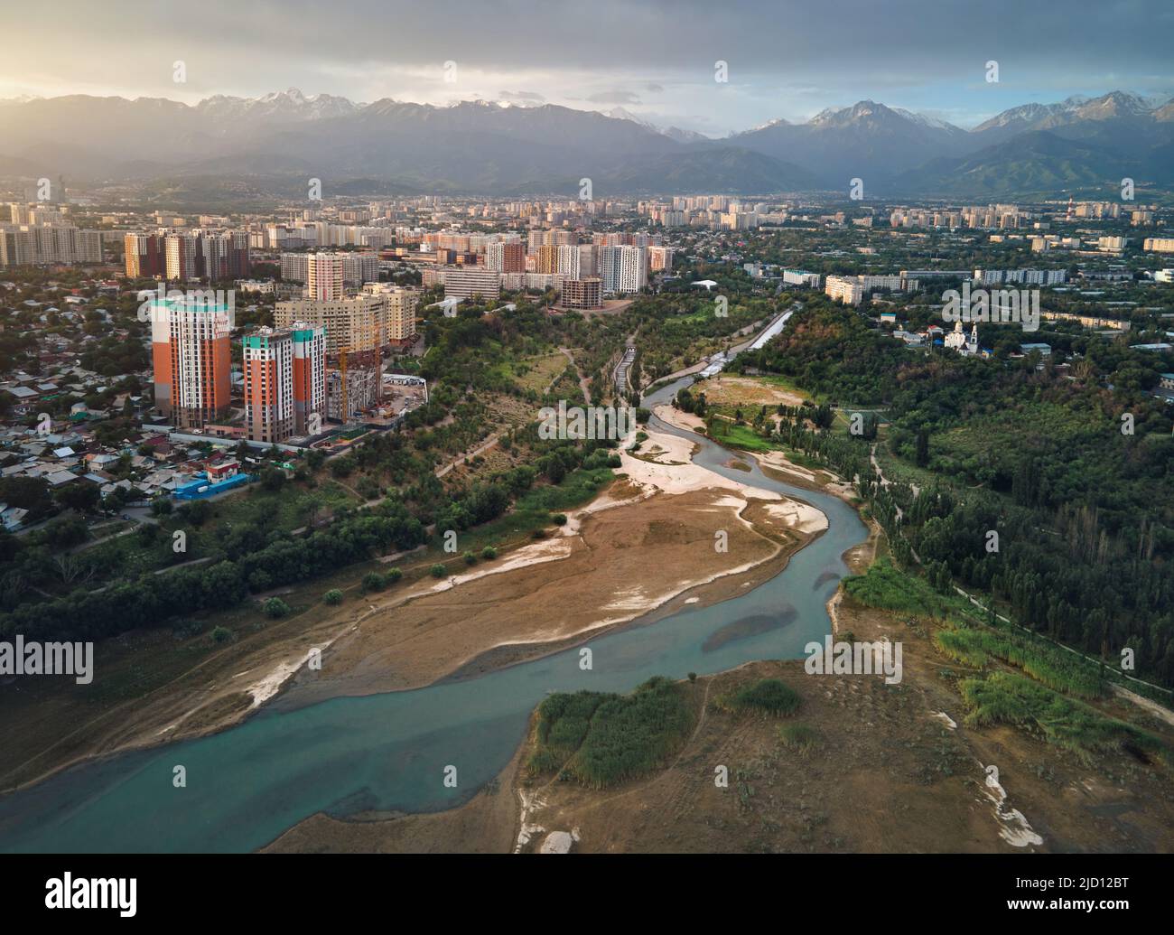 Aerial drone shot of Big Almaty river and Sayran lake with skyscrapers building and snow mountains in Almaty city, Kazakhstan Stock Photo