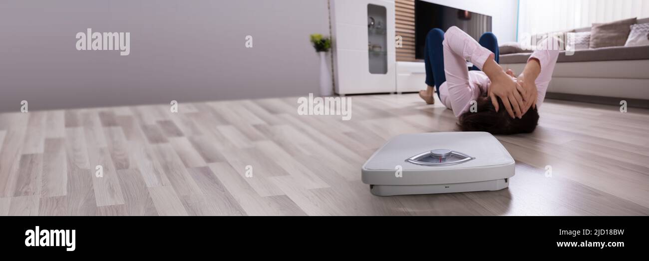 Close-up Of A Weighing Scale Besides Woman Lying On Hardwood Floor Stock Photo