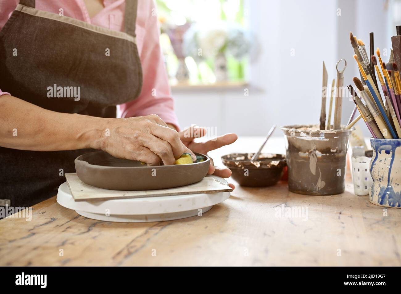 Aged woman making a pottery, drawing some art on her plate in the