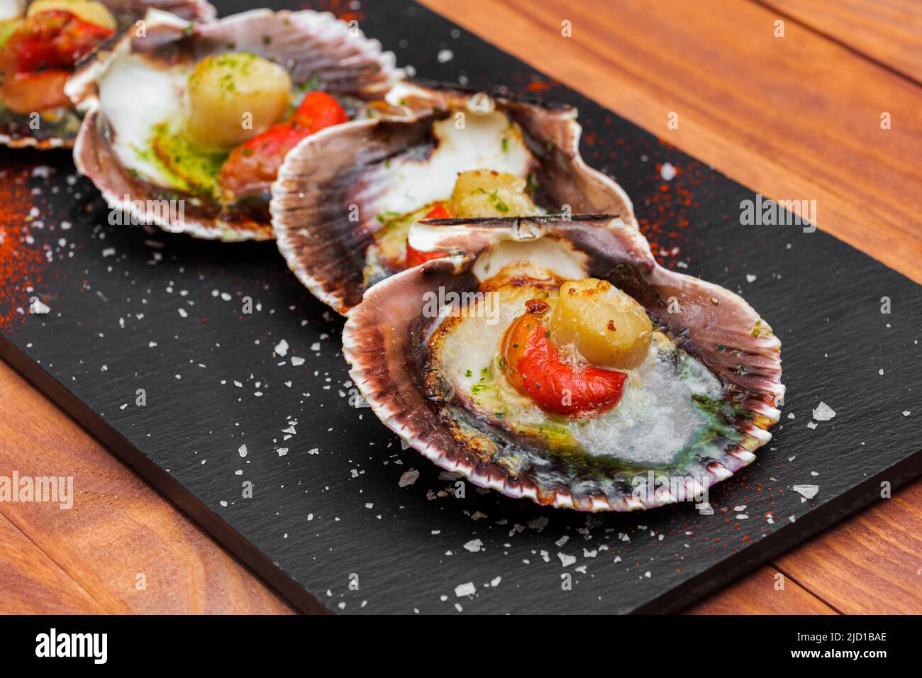 Cooked scallops on blackstone slate plate with species. Variety of