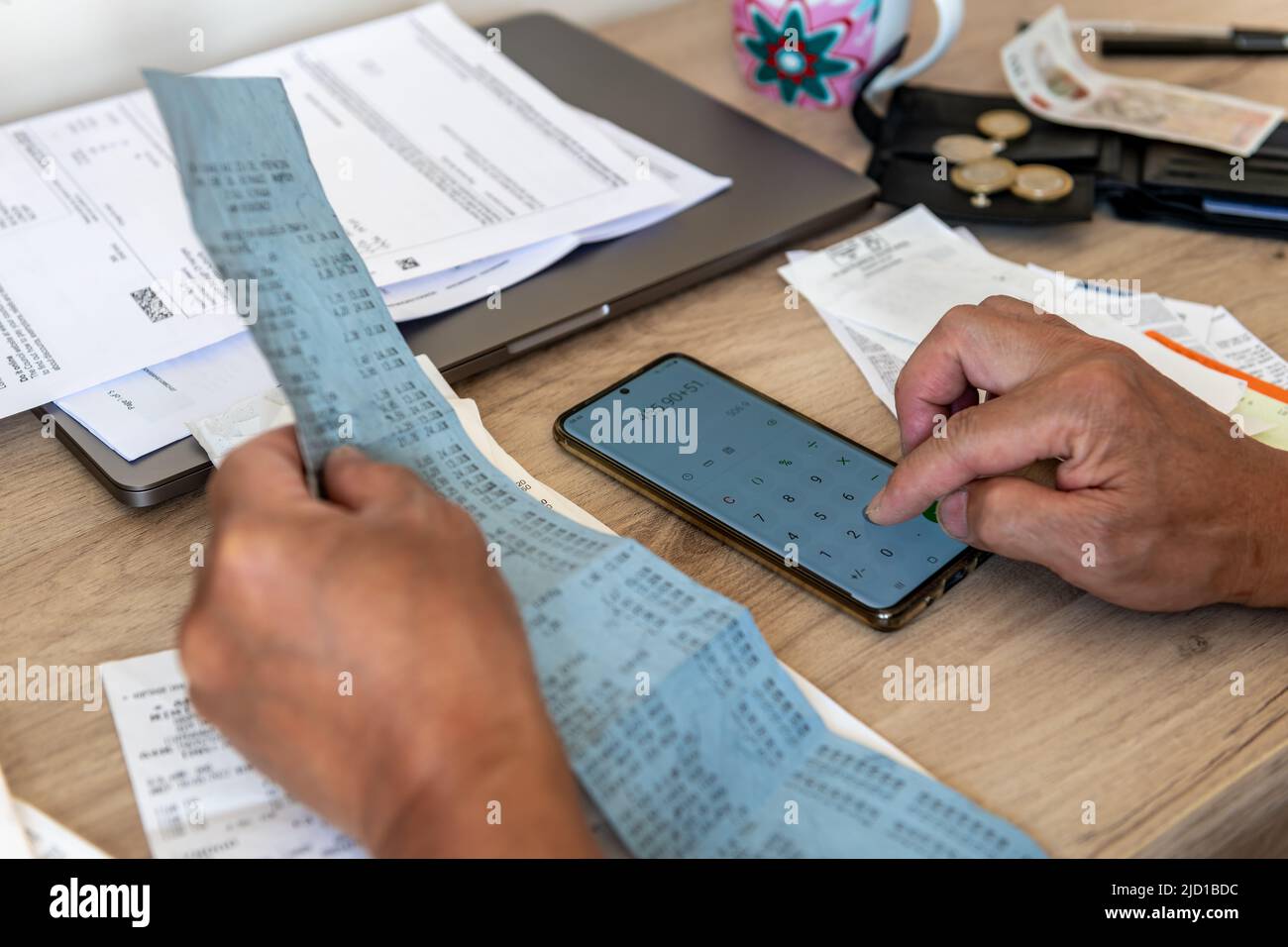 A person calculating the cost of living with a phone calculator and a desk full of bills and till receipts. Stock Photo
