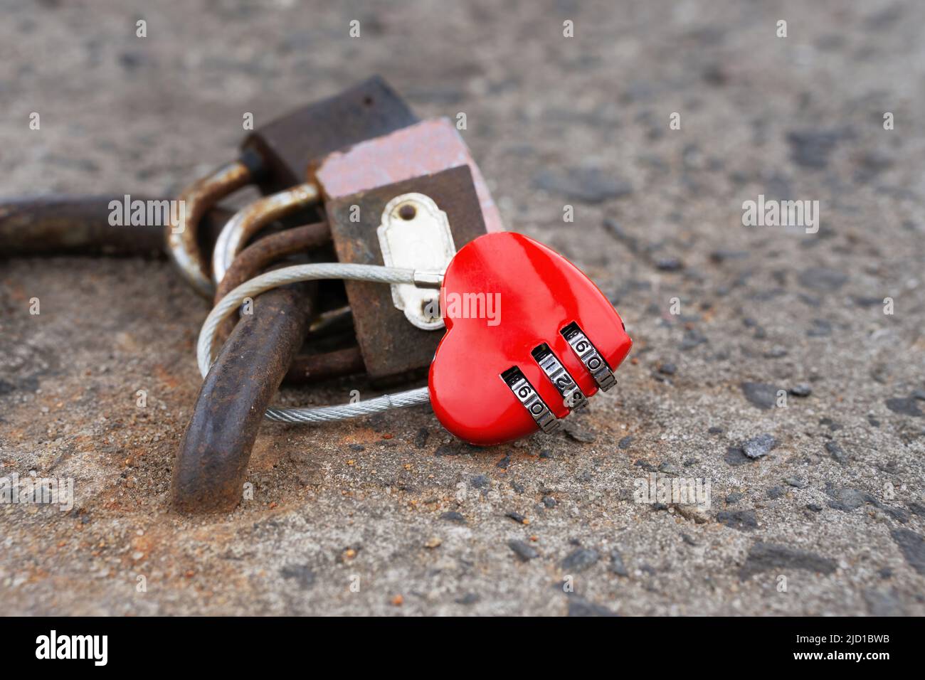 Locked new heart shaped combination wire rope lock among rusty love padlocks outdoors. Strength and constancy of a relationship. Stock Photo
