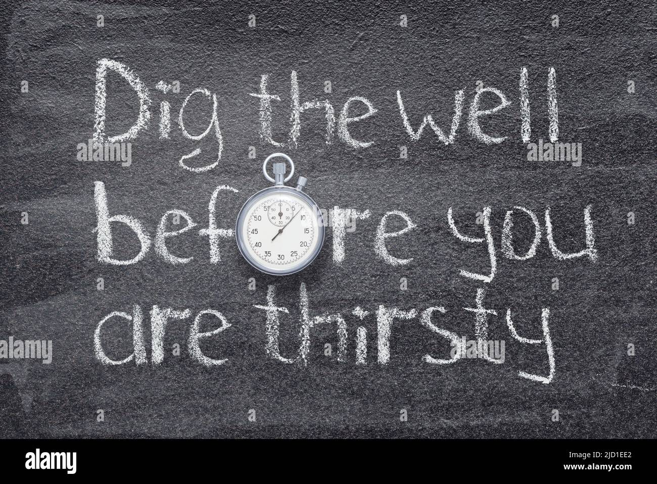 Dig the well before you are thirsty Chinese proverb written on chalkboard with vintage precise stopwatch Stock Photo