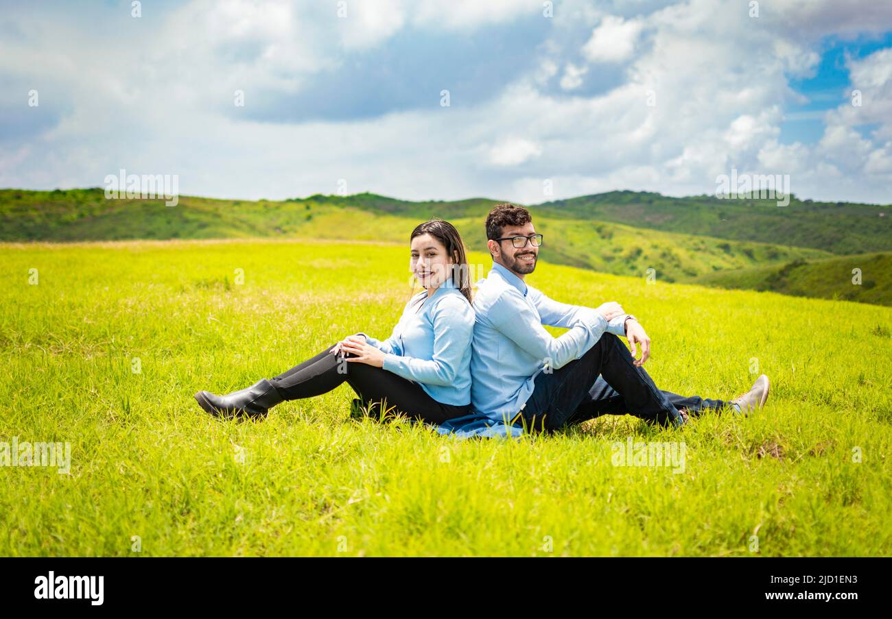 Wedding couple in the field sitting back to back facing the camera, A wedding couple sitting back to back on the grass Stock Photo