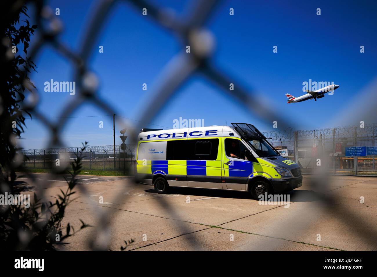 Security fence and a police van at Gatwick Airport as a British Airways plane takes off on the runway Stock Photo
