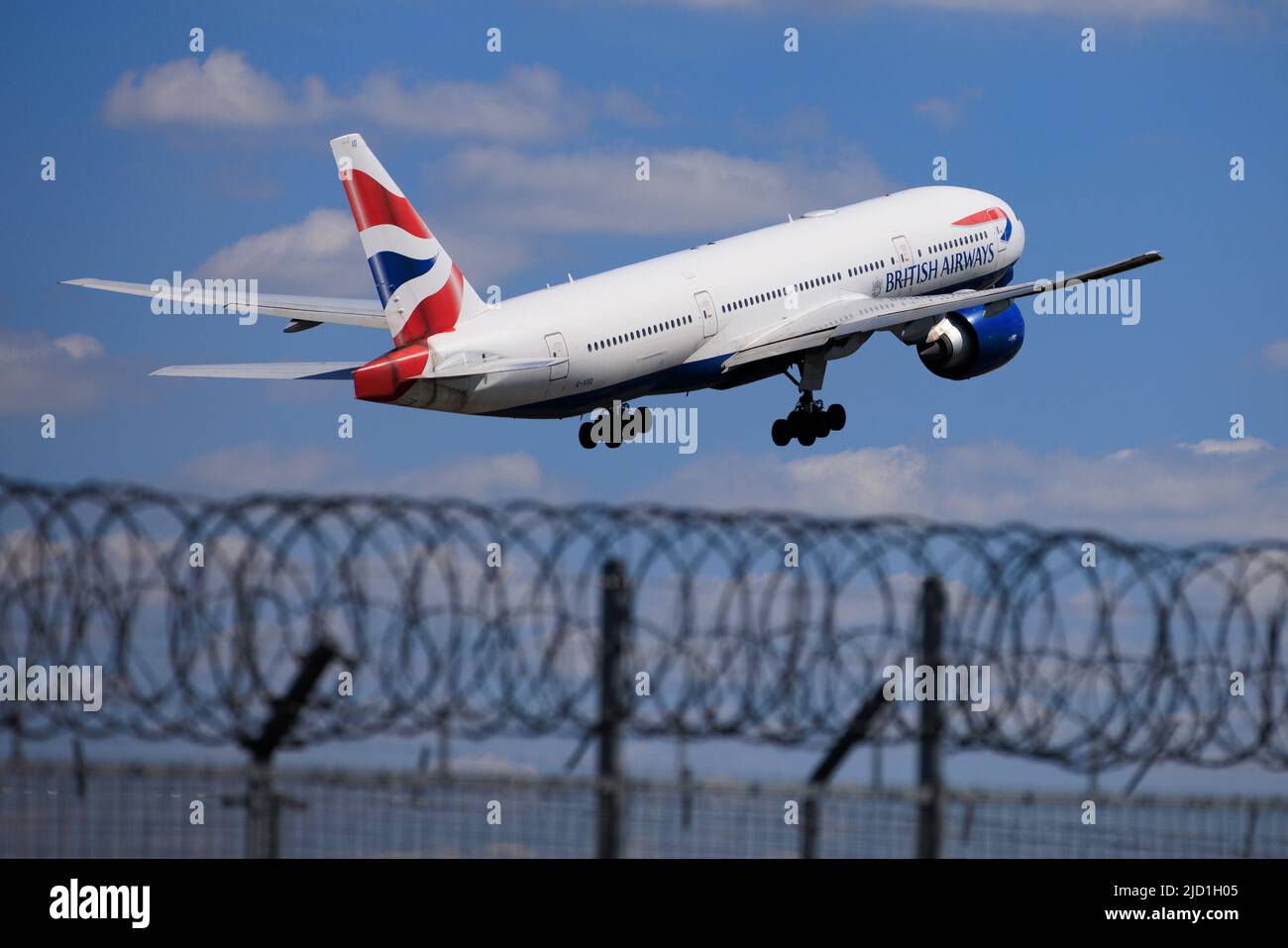 Security fence at Gatwick Airport as a British Airways plane takes off on the runway Stock Photo