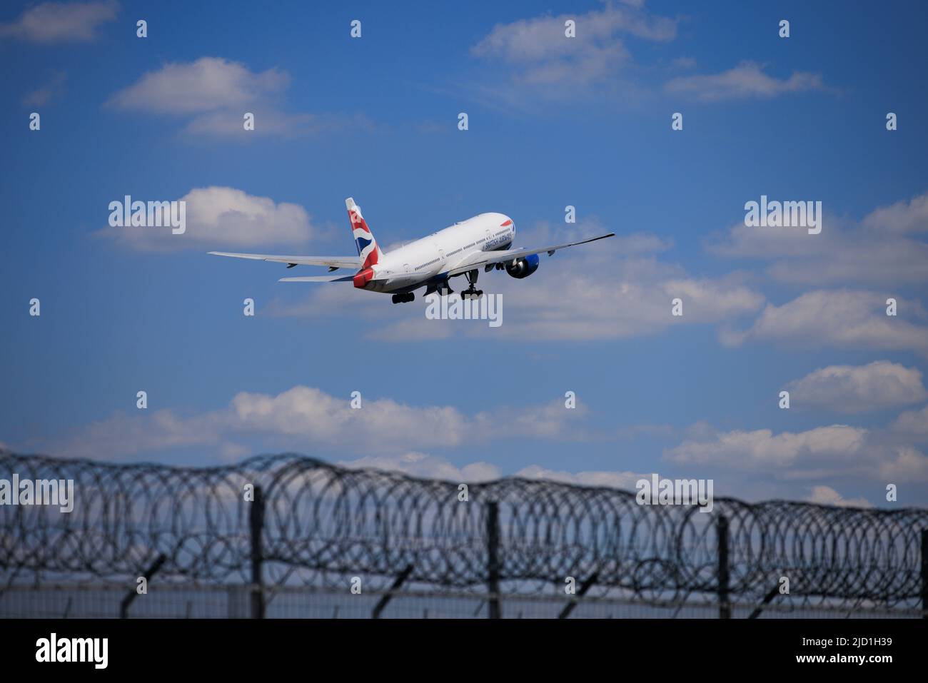 Security fence at Gatwick Airport as a British Airways plane takes off on the runway Stock Photo