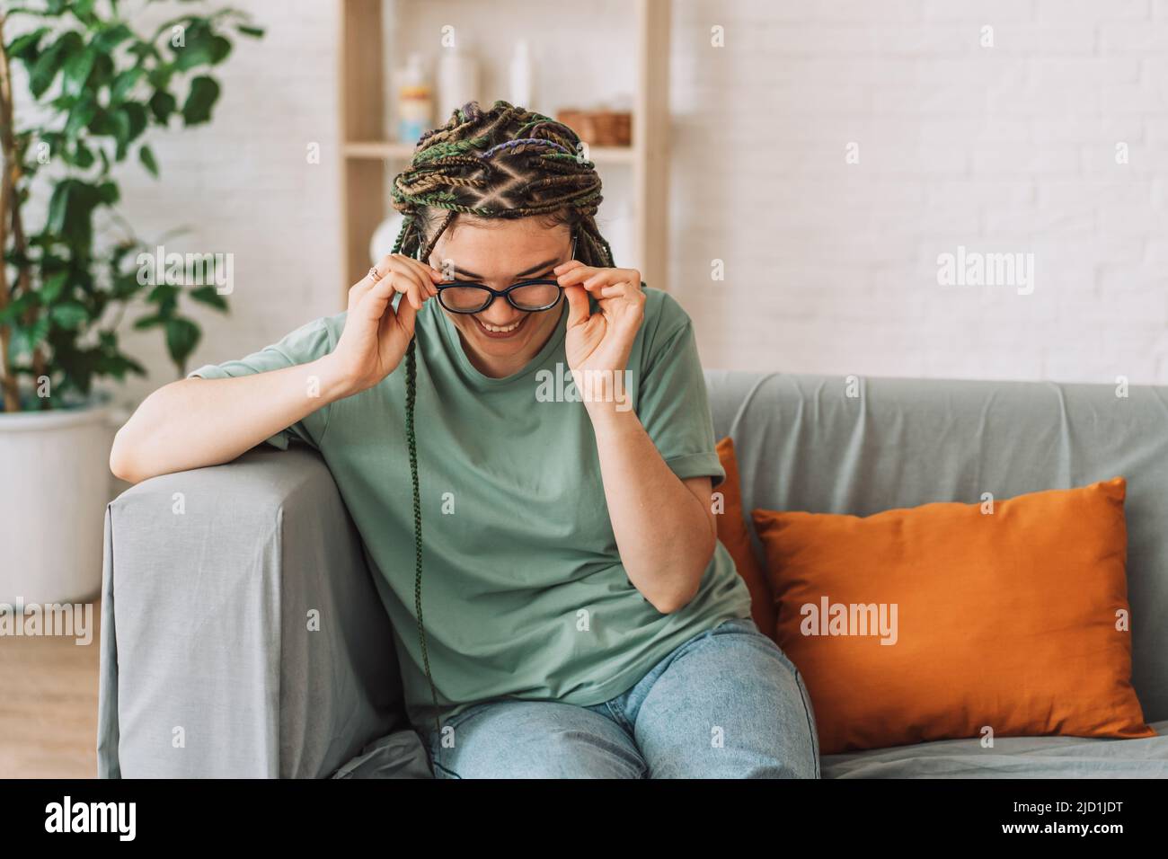 Smiling girl putting on glasses while sitting on the couch Stock Photo