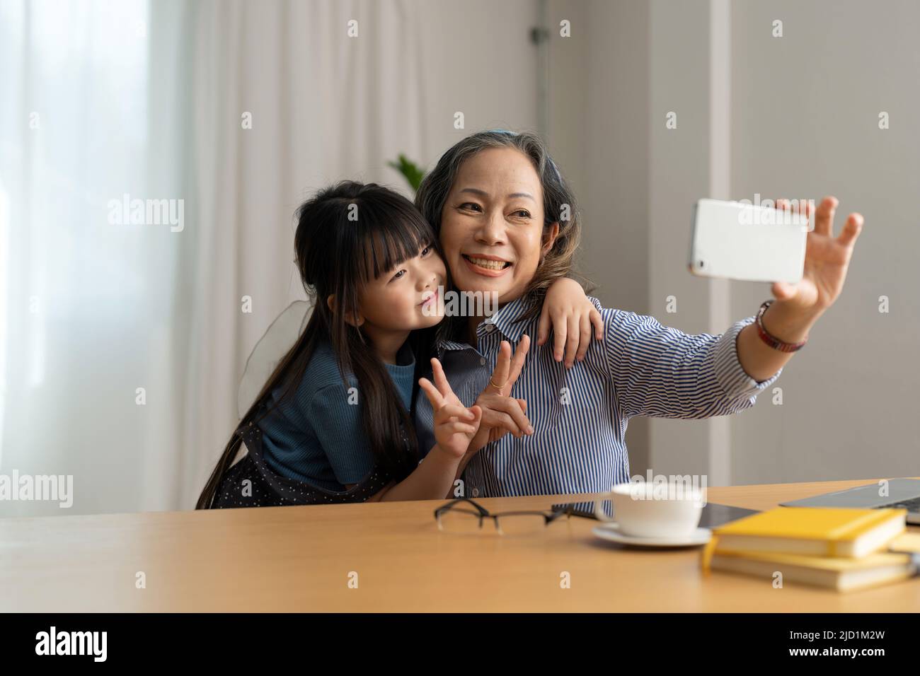 Happy asian smiling older grandma and child girl having fun taking selfie on phone, cheerful granny with little kid play making photo on mobile Stock Photo