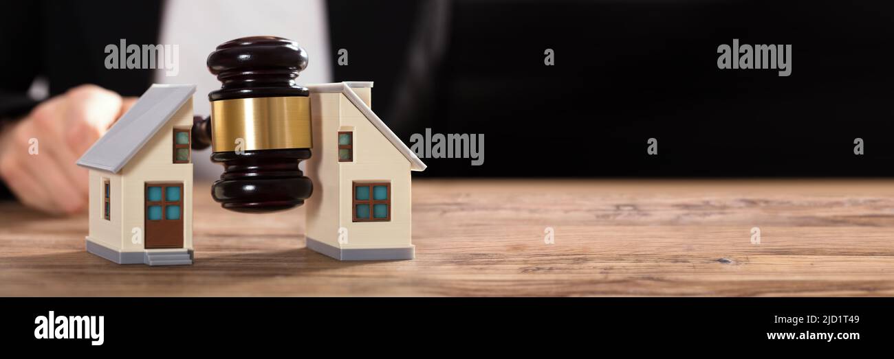 Close-up Of A Judge Striking Gavel Between Split House Over Wooden Desk Stock Photo